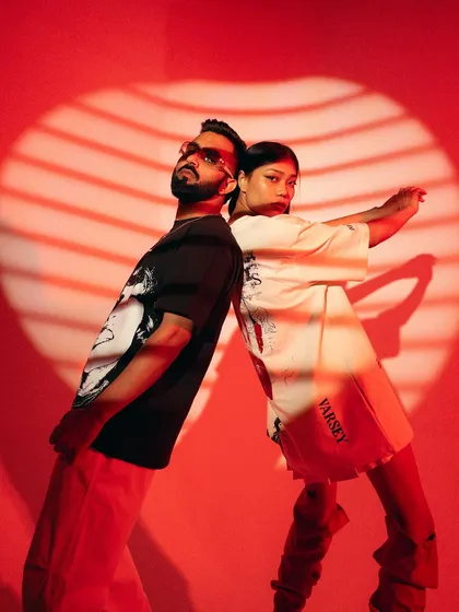 A dynamic back-to-back pose with creative lighting. The shadow patterns add texture and visual interest, making this a standout shot for a streetwear campaign.