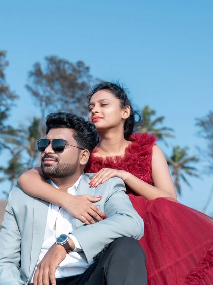 A relaxed and stylish pose on the beach rocks. The bride-to-be looks stunning in a ruffled red gown, enjoying the moment with her partner.