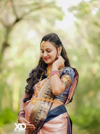 A candid, downward-glancing pose of the mother-to-be, highlighting her intricate jewelry and the texture of her saree.