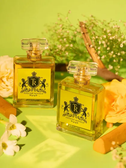 This bright and fresh composition for a floral and woody perfume uses a vibrant green background, yellow roses, and sandalwood sticks. The lighting and props are chosen to visually represent the fragrance notes of the scent.
