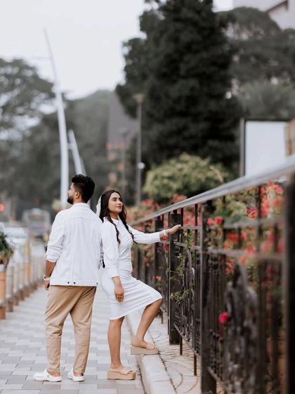 A couple in matching white and khaki outfits looks out from a city bridge, creating a thoughtful and stylish urban portrait.