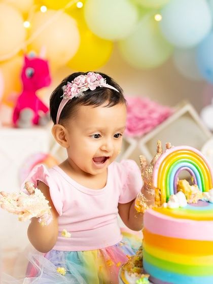 The moment of excitement right before the cake smash begins. Her eyes are wide with anticipation in this colorful rainbow and unicorn themed setup.