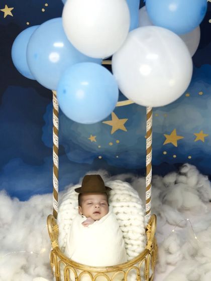 A close-up view of the hot air balloon theme, focusing on the baby swaddled in a white blanket and wearing a little brown hat, ready for a dreamy journey through the starry sky.
