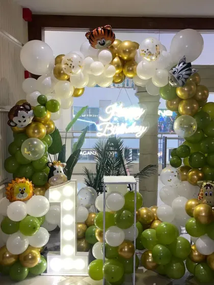 A wild and fun jungle theme for a first birthday party! This setup includes a green, gold, and white balloon arch, cute animal foil balloons, and a light-up number '1'.