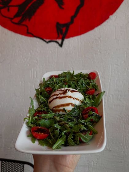 Our burrata salad, held up against our signature red logo. It's as photogenic as it is delicious.