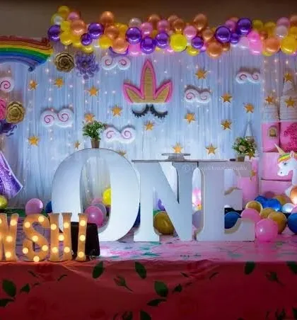 A dreamy unicorn and rainbow themed first birthday, featuring a large "ONE" marquee, unicorn figures, and a pastel rainbow balloon backdrop.
