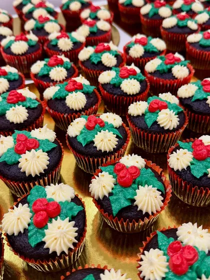 An army of my Christmas-themed cupcakes, ready for a holiday party. Each one is a moist Belgian chocolate cupcake with vanilla buttercream frosting, decorated with holly and berries.