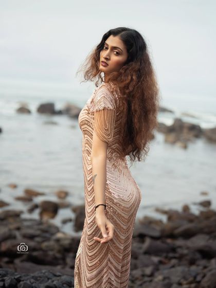A beautiful portrait of the model looking back over her shoulder, with her sequined dress catching the last rays of sunlight. The image has a warm, golden-hour glow.