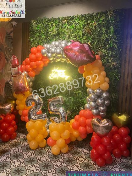 A full view of the makeup themed 25th birthday, showing the complete circular balloon arrangement against the artificial green wall.