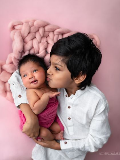 A big brother gives his newborn sister a sweet kiss. These are the unscripted, loving moments that make sibling portraits so special.