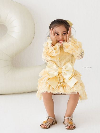 Peek-a-boo, I'm two! This little girl's playful expression is priceless as she celebrates her second birthday in a beautiful yellow lace dress.