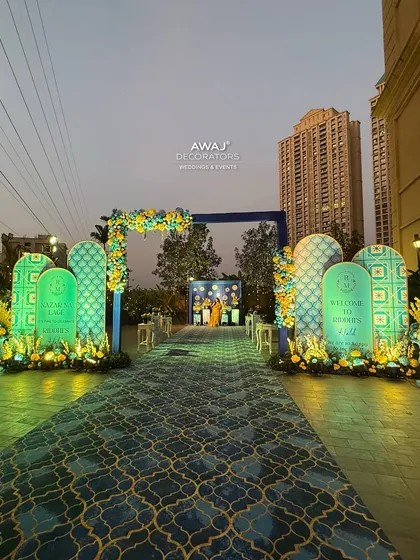 The Haldi entrance illuminated at dusk, with uplighting creating a beautiful glow on the patterned backdrops and floral decor.