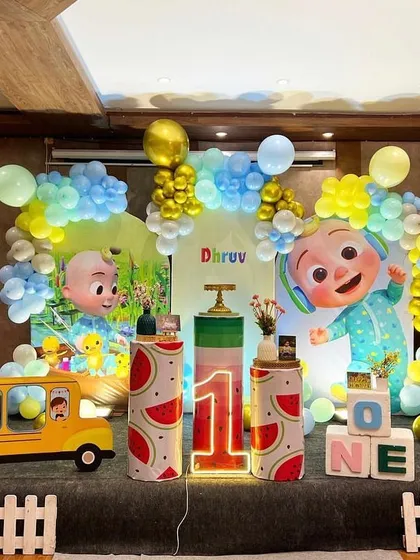 Here is a vibrant Cocomelon themed first birthday party. The setup includes large character cutouts, a custom backdrop, themed pedestals, and a light-up number '1' to bring the popular show to life.