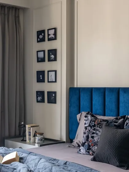 A bedroom from our award-winning 'Maison-De-Confort' project, featuring a bold blue velvet headboard and a gallery wall of black-and-white photos.