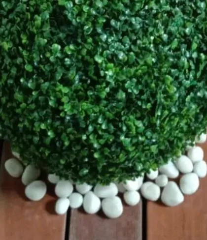 A close-up of a decorative artificial boxwood ball placed on white river stones. These small details add a polished and curated feel to our garden designs.