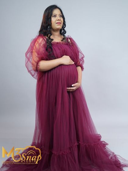 An elegant maternity portrait featuring a beautiful flowing gown in a rich magenta color. The soft fabric and classic pose create a look of timeless grace.