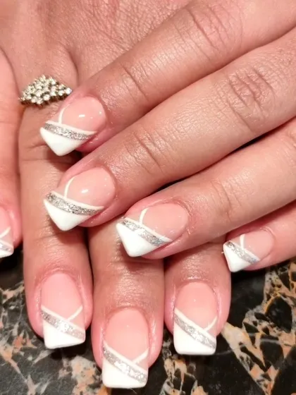 A clean and geometric design with white tips and intersecting silver glitter lines on short, square nails.