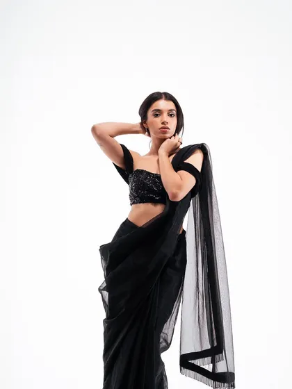 A graceful and elegant pose in a studio. The model's posture highlights the off-shoulder design of the blouse and the drape of the saree, creating a timeless fashion portrait.