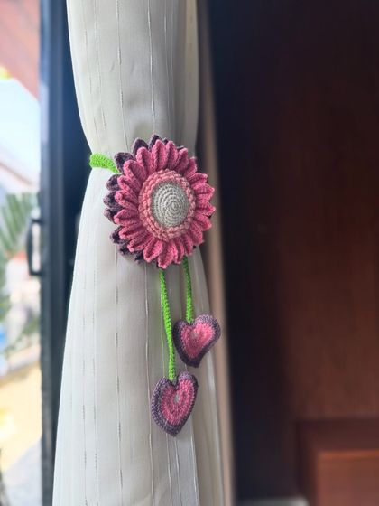 A beautiful, custom-colored sunflower tie-back in shades of pink. The dangling hearts add an extra layer of charm to this floral design.