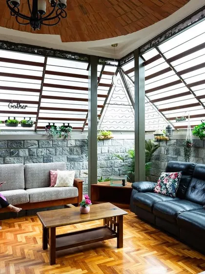 We dissolve the boundaries between inside and out. This living area uses expansive slatted windows and a stone accent wall to create a serene space that feels like a sheltered extension of the garden, filled with natural light and air.