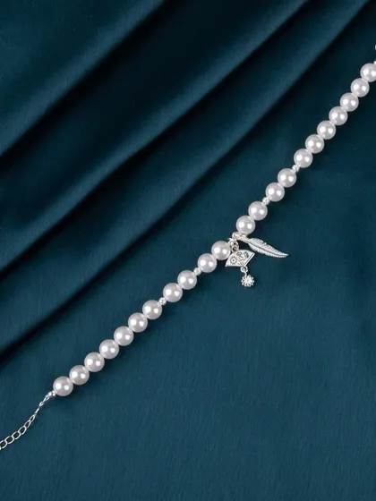 A pearl bracelet with a silver feather charm, shot on dark fabric.