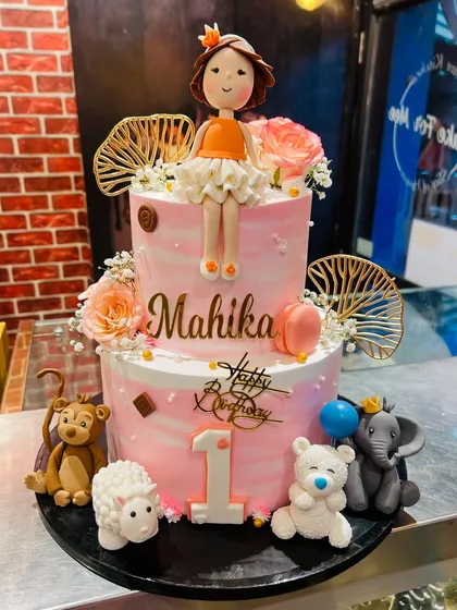 A two-tier first birthday cake with a doll topper and an assortment of cute fondant animals.