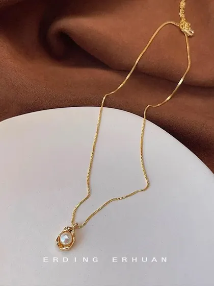 A unique necklace featuring a single pearl nestled inside a textured, nest-like gold-tone pendant. A beautiful and artistic design.