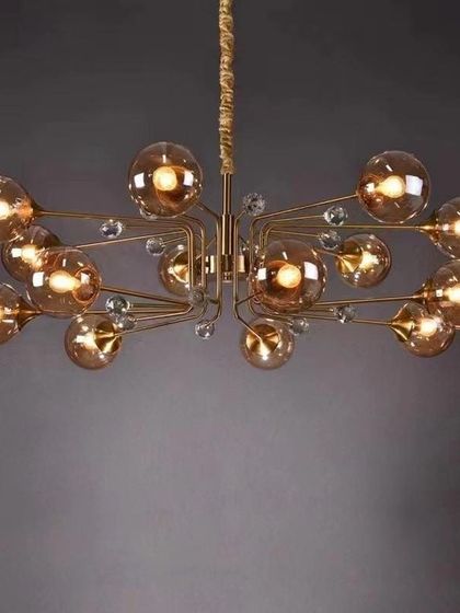 A modern brass chandelier featuring amber glass globes extending from a central frame. This global pendant light offers a warm, ambient glow and a stylish, retro-inspired look for a dining or living area.