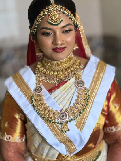 This is the traditional South Indian 'Goddess' look that I love creating for the Muhurtham. For Harshitha, we went with bold, 3D eyes and a classic red lip to complement her stunning gold jewelry and white Kanjivaram saree.