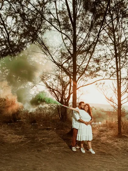 A couple embraces as a cloud of colorful smoke billows around them. Using smoke bombs is a great way to add a vibrant and dramatic element to your pre-wedding photography.