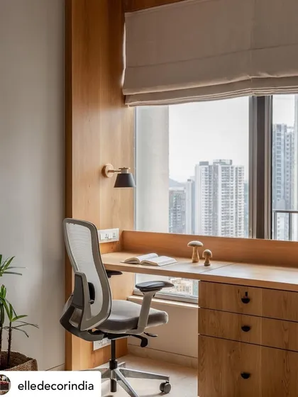 A dedicated home office space with a view. The light wood desk and ergonomic chair are set against a backdrop of the city, creating an inspiring and functional work-from-home environment.
