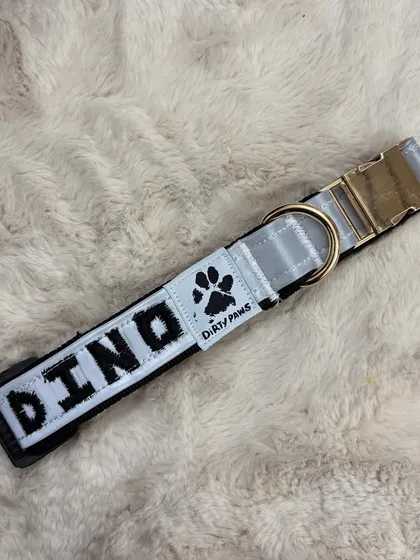 A close-up view of a custom reflective collar with the name "DINO" embroidered on it, resting on a soft, plush surface. I can personalize your pet's collar to make their safety stylish.