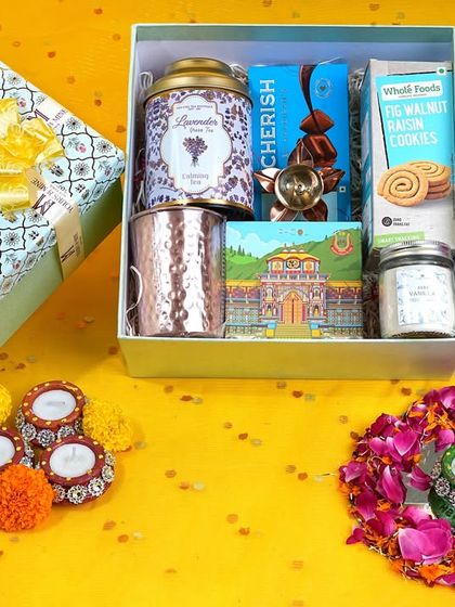 A top-down creative shot of a gift hamper, styled with flowers and diyas on a bright yellow background. This vibrant flat lay is designed to grab attention on social media.