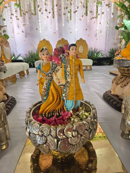 A beautiful centerpiece featuring dolls representing the couple, placed in a silver floral bowl.