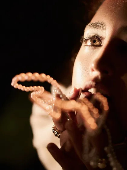 An abstract, artistic close-up where a pearl necklace is blurred in the foreground, drawing the viewer's eye to the model's intense gaze. This technique adds depth and tells a story beyond just showcasing the accessory.