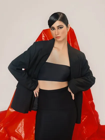 A confident, hands-on-hips pose that showcases a modern, minimalist black outfit. The red background adds a pop of energy and power.