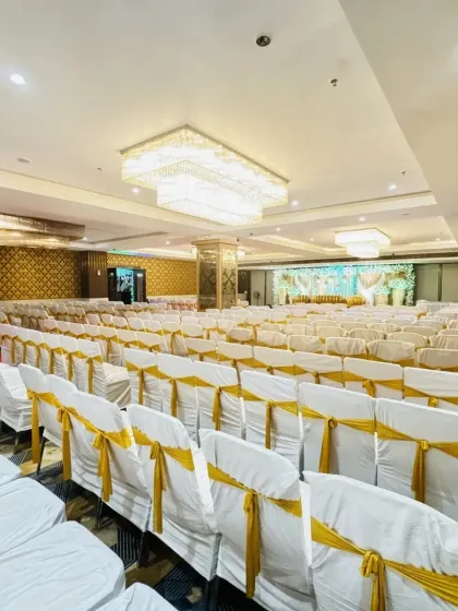 A wide view of a banquet hall in Vashi, set up with white and gold themed seating. The large crystal chandeliers add a luxurious feel to the entire space.