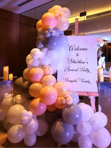 A personalized welcome sign for the arrival party, set on an easel and surrounded by a beautiful organic balloon arrangement. Mirrored pedestals with candles add a touch of elegance.