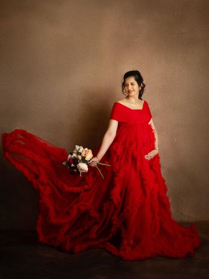 The flowing train of the red gown creates a beautiful sense of movement in this studio shot. The mom-to-be’s happy expression completes this dynamic and joyful portrait.