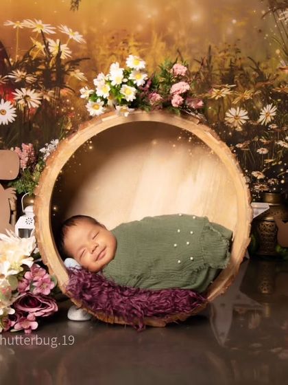A sweet smiling newborn, wrapped in a green swaddle, sleeps in a bark bowl. The background is a magical jungle scene filled with friendly animal toys.