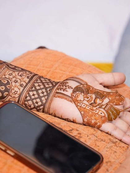 A candid shot of me personalizing a bride's mehendi with a dulha-dulhan figure, with her phone nearby for design reference.
