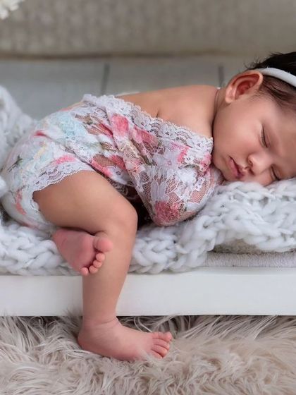 A newborn baby girl in a floral lace outfit, sleeping on her tummy in a miniature white bed. This pose is perfect for showing off cute outfits.