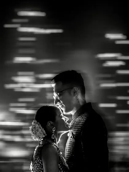 A black and white portrait using a slow shutter speed to create a dynamic, light-streaked background. The effect suggests a world in motion while the couple remains the calm center.