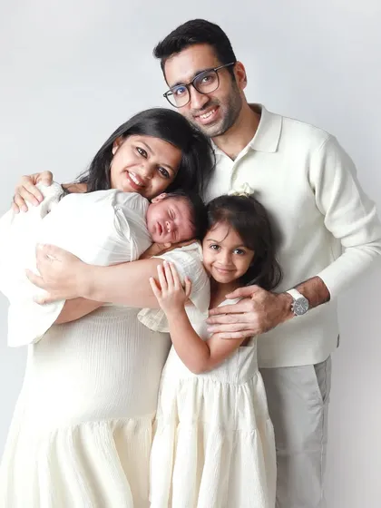 A picture-perfect moment of a family of four. The coordinated white outfits and the genuine smiles create a beautiful, cohesive portrait that celebrates the arrival of their newest member.