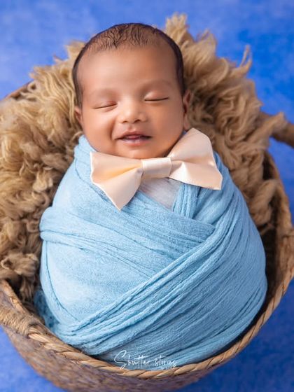 A smile in his sleep. This little gentleman is dressed in a blue swaddle with a tiny bow tie, looking absolutely adorable and content in his basket.