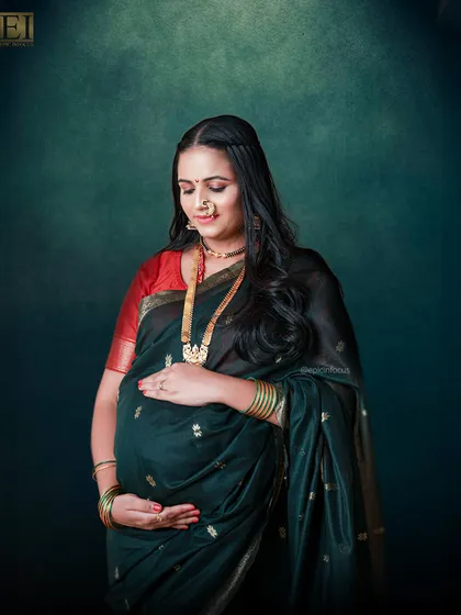 A beautiful portrait of a mom-to-be in a traditional dark green saree with a red border, complete with a classic nose ring and gold jewelry.