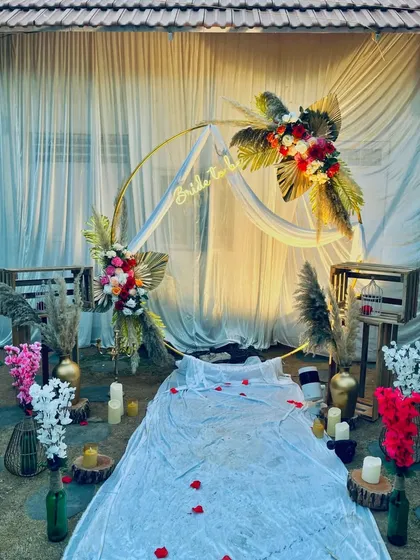 A beautiful "Bride to be" setup with a bohemian flair. A golden circular arch is decorated with dried palms and florals, with a low, fabric-draped seating area on the ground for a relaxed and stylish celebration.