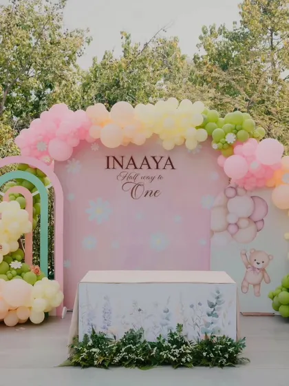 A gorgeous pastel rainbow setup for Inaaya's half-birthday celebration, featuring arched backdrops and a floral-covered table.