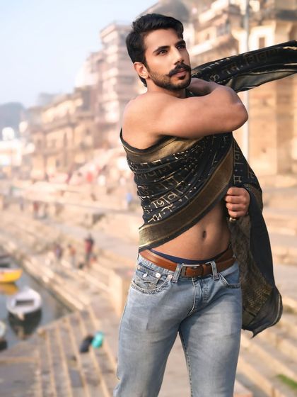 A candid, powerful portrait showing the subject adjusting his drape, with the bustling life on the Ganga blurred in the background.