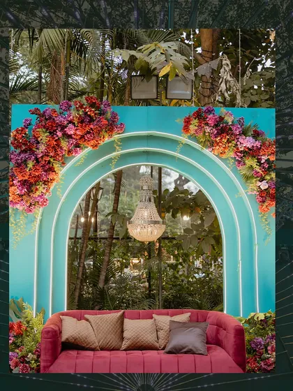 A vibrant photo booth at the Sangeet, with a turquoise arch, a plush red sofa, and a dramatic chandelier. I love using bold color contrasts to create memorable decor moments.